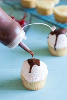 someone pouring chocolate on top of some cupcakes