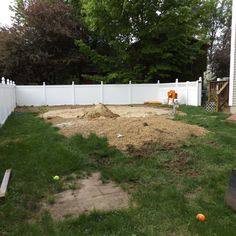 a yard with grass and dirt in front of a white fenced in backyard area