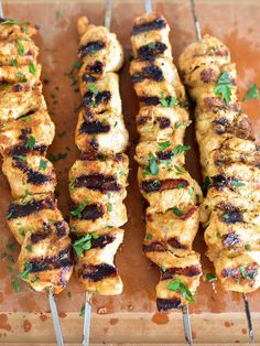 four skewers of chicken on a wooden cutting board