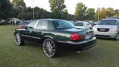 a black car parked on top of a lush green field next to other cars in a parking lot