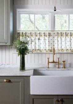 a white kitchen sink sitting under a window next to a vase with flowers in it