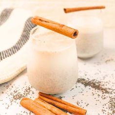 two glasses filled with milk and cinnamon sticks on a towel next to some sugar sprinkles