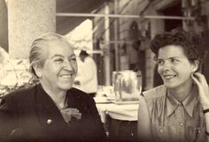 an old photo of two women sitting next to each other in front of a table