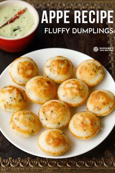 a white plate topped with puffy dumplings next to a bowl of dipping sauce