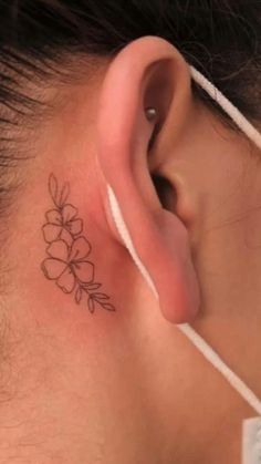 a woman's behind the ear has a small flower tattoo on her left side