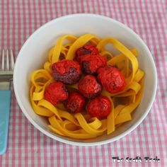 a white bowl filled with pasta and meatballs on top of a pink checkered table cloth