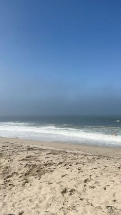 a person is walking on the beach with a surfboard in their hand and another person swimming in the ocean behind them