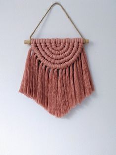 a pink wall hanging with tassels attached to it's sides on a white wall