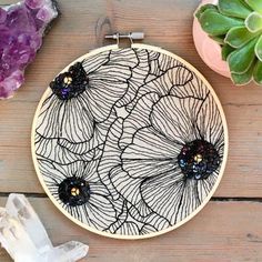 an embroidery project with black and white flowers on it, surrounded by crystal crystals in front of a succulent plant