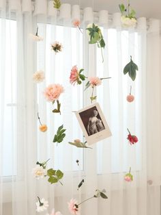 flowers are hanging from the ceiling in front of a window with sheer drapes and curtains