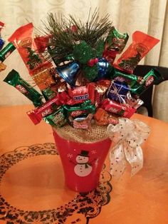 a cup filled with assorted candy on top of a wooden table next to a christmas tree