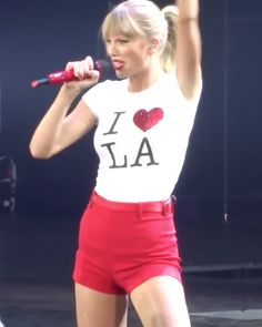 a woman in red shorts and a white t - shirt holding a microphone up to the air