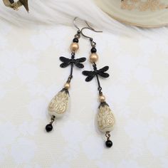 These unique handmade earrings were created by me with unique teardrop shaped acrylic beads in cream with metallic gold accents.  To these I wired pretty detailed matte black plated brass dragonfly charms, gold and black crystal cored high quality pearls, and additional antiqued brass metal accents.  These are 3 1/2 inches long total including the brass hook ear wires.  The widest point of the dragonfly wings measures 3/4 inch across. Thank you for viewing my listing - to see more please click here to visit my shop homepage:  www.etsy.com/shop/hhjewelrydesigns Dark Cottagecore Aesthetic, Goth Earrings, Unique Handmade Earrings, Antique Brass Metal, Victorian Goth, Dragonfly Charm, Cottagecore Aesthetic, Cream And Gold, Metallic Accents