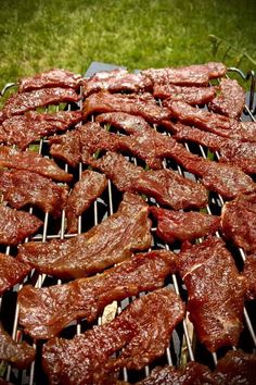 steaks and ribs cooking on a grill in the grass with tongs sticking out