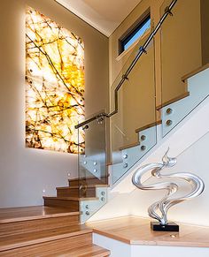 a staircase with glass railings next to a painting on the wall and wooden steps