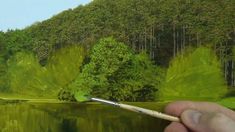 a person is holding a paintbrush in front of a painting of trees and water