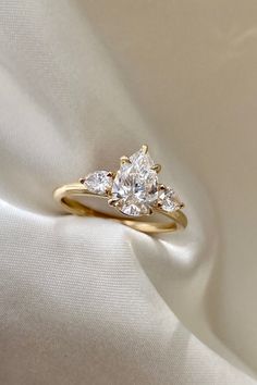 a three stone diamond ring sitting on top of a white cloth