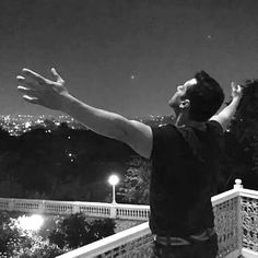 a man standing on top of a balcony next to a lush green hillside at night