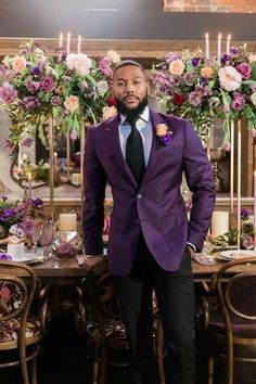 a man in a purple suit standing next to a table with flowers and candles on it