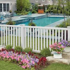 a white picket fence with flowers in the foreground and a pool in the background