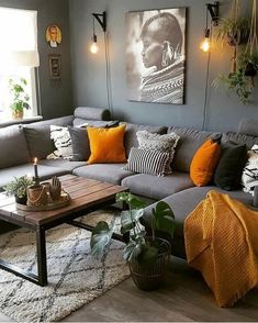 a living room with grey couches and orange pillows on the floor, plants in vases