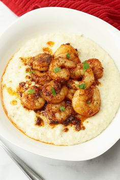 a white bowl filled with grita and shrimp on top of a table next to a fork