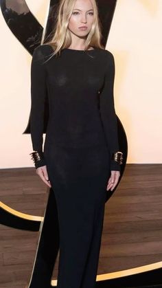 a woman in a black dress standing on a wooden floor with her hand on her hip