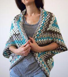 a woman is wearing a crocheted shawl and standing in front of a white wall