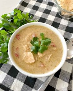 a white bowl filled with soup and garnished with cilantro on a checkered table cloth