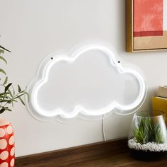 a white cloud shaped neon sign sitting on top of a wooden table next to a potted plant