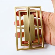 a hand holding a gold metal object with squares and rectangles on the sides