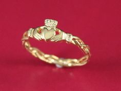 a gold ring with a heart and two hearts on the side, sitting on a pink surface