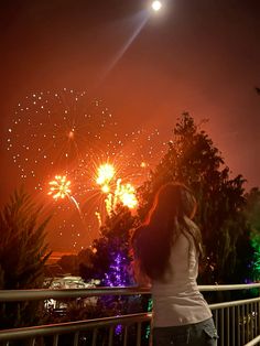 a woman standing on a balcony watching fireworks go off in the night sky above her