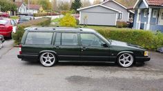 a green station wagon parked in a parking lot next to some houses and cars on the street