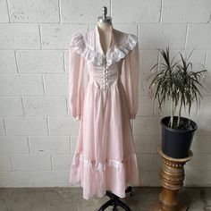 This 1970's vintage Gunne Sax dress from the Romantic Renaissance Bridal Collection is made from a pastel pink colored cotton blend and white, floral lace. Features a band collared, puffy sleeved, fit and flare, tie waist, maxi length fit with eyelet button closures down the front of the bodice. Zips up in back with a Talon zipper. In excellent vintage condition with little to no signs of wash or wear No size listed, see below for measurements 15" shoulders 32" chest 26" waist untied 50" hips 50" length 23" sleeve length Vintage Dress With Fitted Bodice, Feminine Victorian Dress For Spring Garden Party, Spring Victorian Dress With Ruffles For Garden Party, Feminine Victorian Dress For Garden Party In Spring, Daywear Prairie Dress With Ruffled Fitted Bodice, 1970s Ruffled Vintage Day Dress, Feminine Ruffled Dresses For Vintage Fashion, Feminine Vintage-style Ruffled Dresses, Feminine Vintage Fashion Dresses With Ruffles