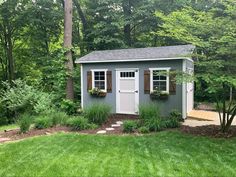 a small shed in the middle of some trees and grass with windows on each side