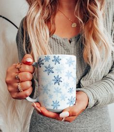 a woman holding a coffee mug with snowflakes on the outside and inside it