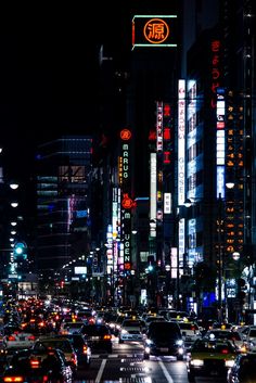 a city street filled with lots of traffic next to tall buildings and neon signs at night