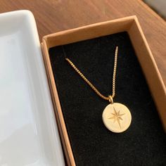 a gold necklace with a star on it sits in a box next to a plate