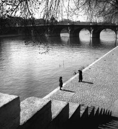 black and white photograph of two people standing on the edge of a bridge over water