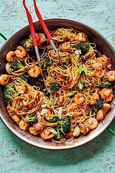 a pan filled with shrimp and noodles on top of a blue wooden table next to chopsticks