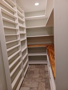 an empty walk in closet with white shelves and wood flooring on the side wall