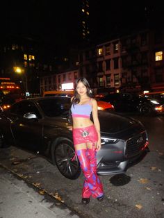 a woman standing in front of a car on the side of the road at night