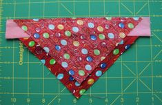 a red dog bandana with polka dots on it sitting next to a green cutting board