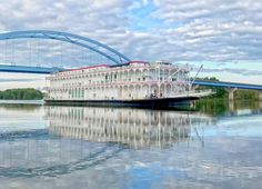 a large boat floating on top of a river next to a blue bridge over water