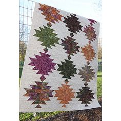 a quilt hanging on a fence in the grass with trees in the back ground behind it