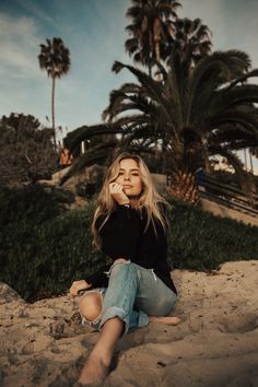 a woman sitting on the sand with palm trees in the background