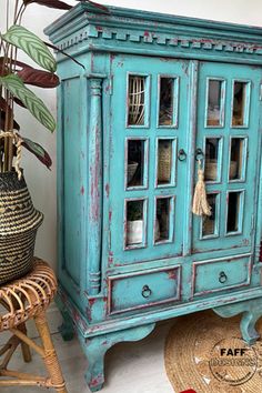 a blue cabinet sitting next to a wicker chair and potted plant on top of a rug