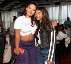 two young women standing next to each other in front of a room full of people