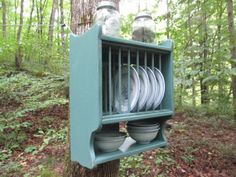 a green shelf with plates and jars on it next to a tree in the woods